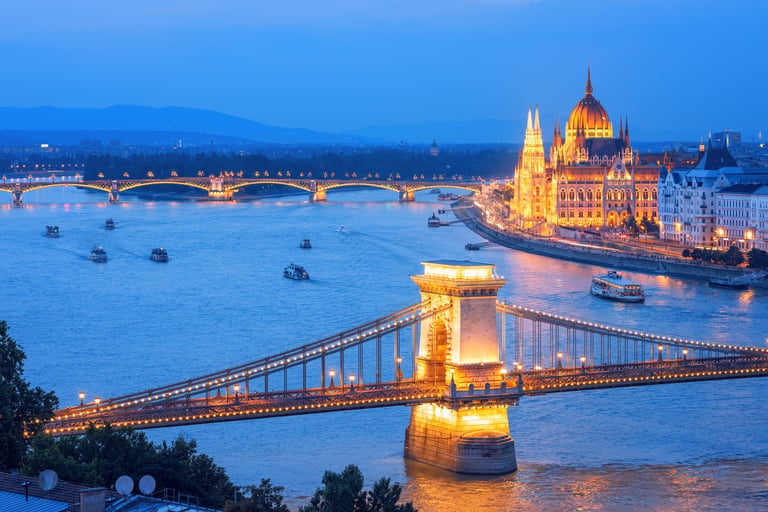 Budapest tourist boats cruising on Danube river along the Chain bridge and Parliament building on a blue evening