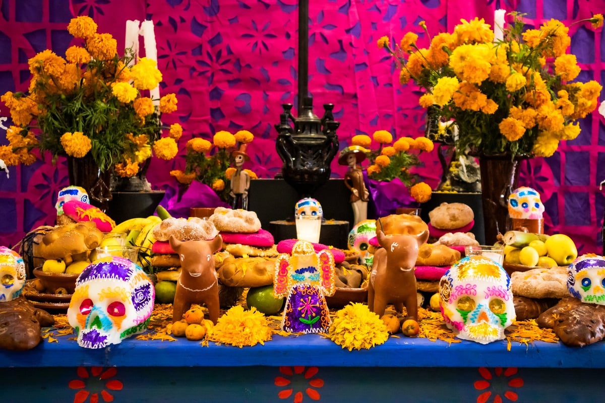 Altar de Día de Muertos con figuras de barro, cempasúchil, pan de muerto, calaveras de azúcar y velas, en una composición llena de color y tradición.