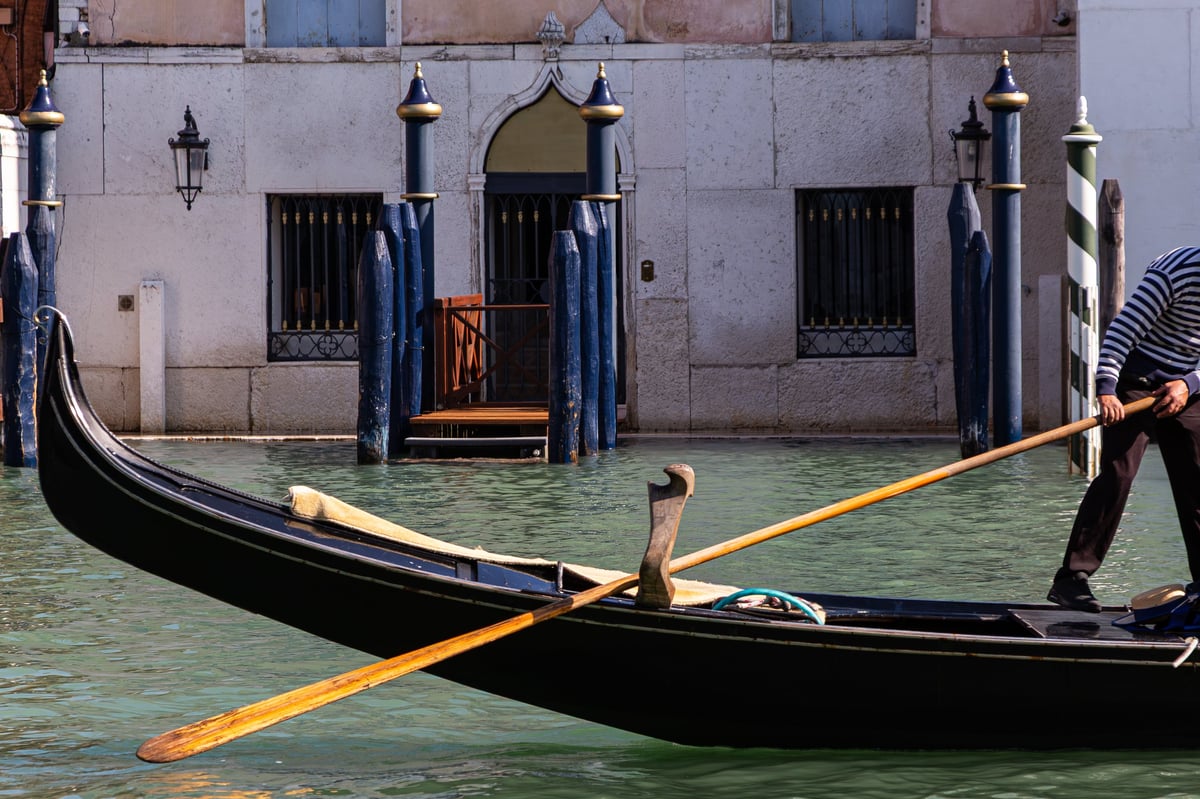 A gondolier in a striped shirt steers his traditional black gondola in a Venetian canal on a sunny day