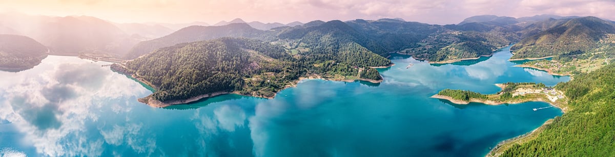 Vista aérea de laguna turquesa entre montañas y bosque de pino