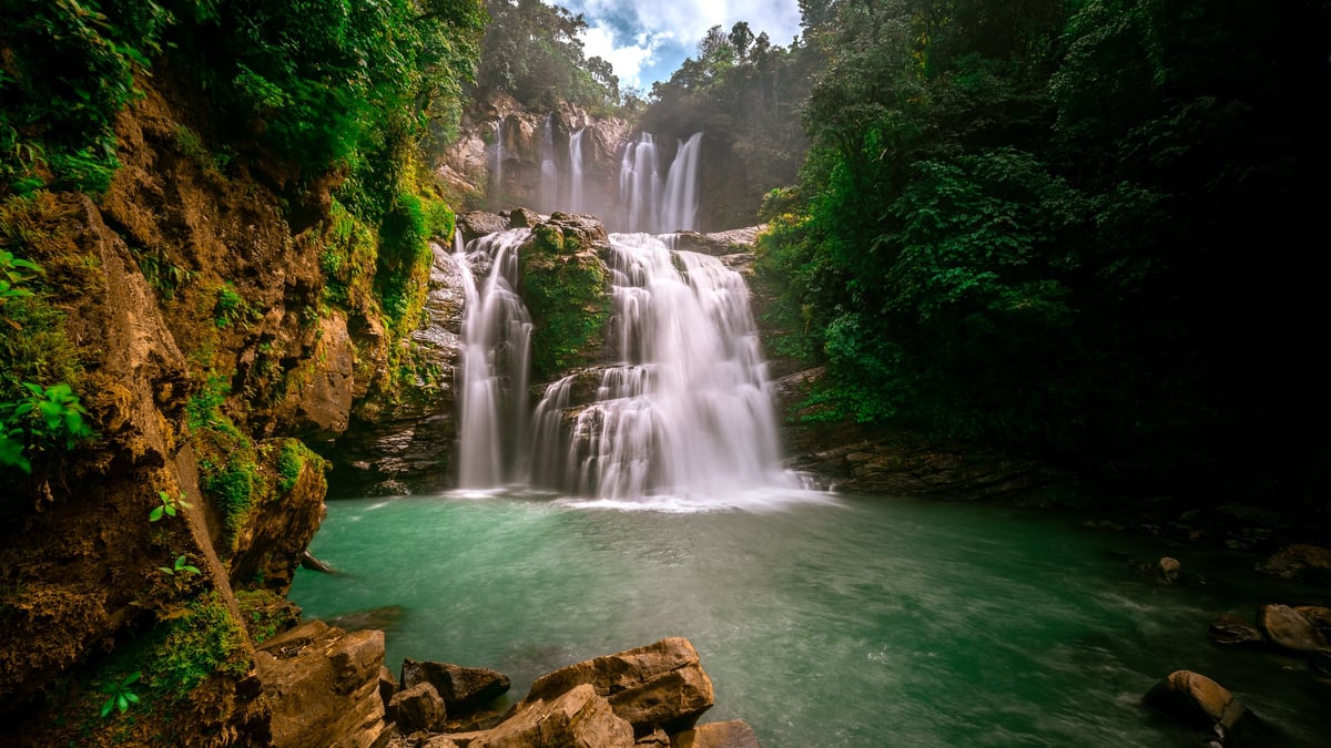 Cascada espectacular de agua turquesa cayendo entre vegetación tropical