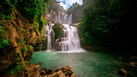 Beautiful waterfall with turquoise water falling amid tropical vegetation, bright blue sky and full sunlight.