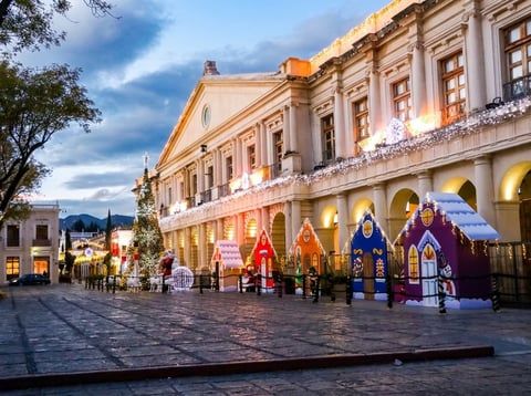 Colonial-era building with ornate yellow facade decorated for Christmas with nativity scene in courtyard at dusk