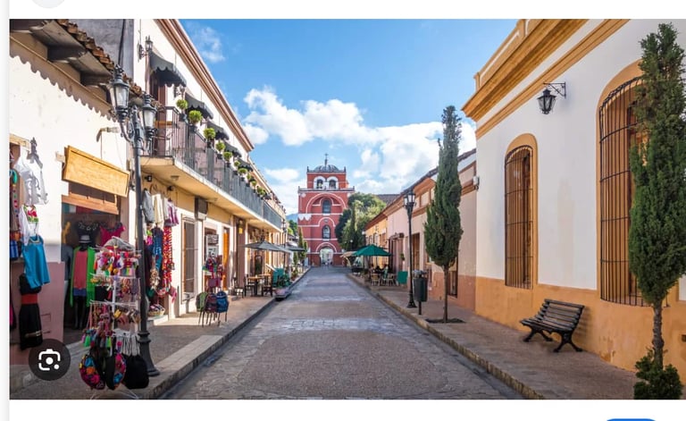 Colorful colonial street in a Mexican town with a pink church tower at the end, lined with shops and colonial architecture