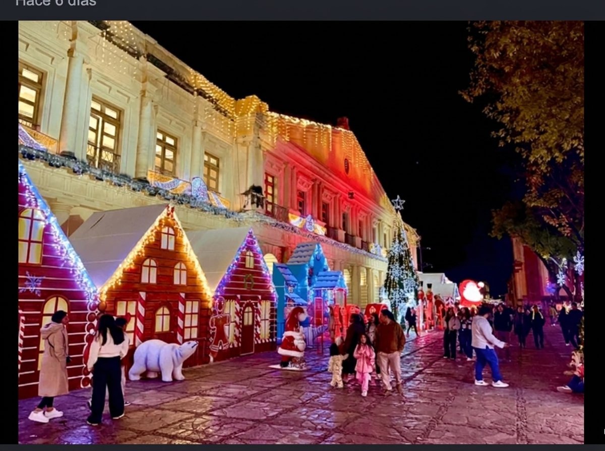 Festive holiday market at night with illuminated gingerbread house decorations and colorfully lit historic building in background