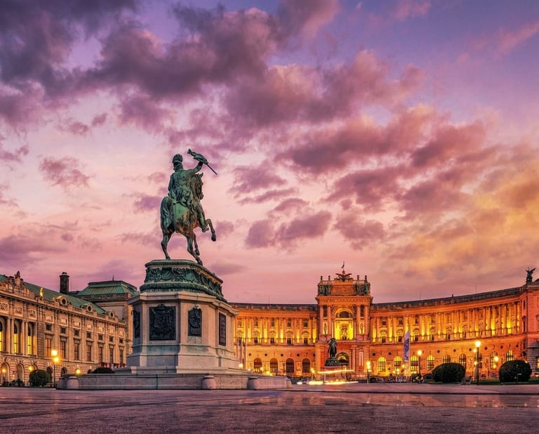 Equestrian statue in Vienna square at dusk with illuminated historic buildings and purple-pink sunset sky
