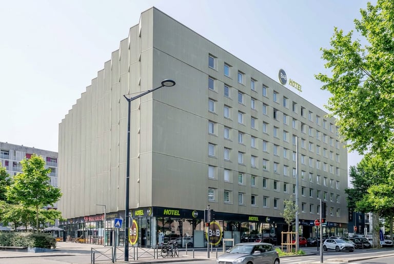 Edificio de apartamentos moderno gris con locales comerciales en planta baja y árboles en esquina urbana