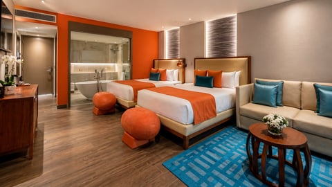 Habitación de hotel moderna con paredes naranjas, cama king, ottoman naranjas, sofá con cojines azules y piso de madera