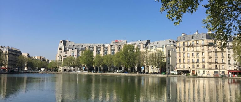 Parisian waterfront with Haussmann-style apartment buildings reflected in calm canal water under blue sky