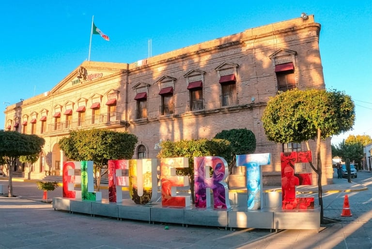 Colorful IMAGINE sculpture in front of historic sandstone government building with flag and green hedges