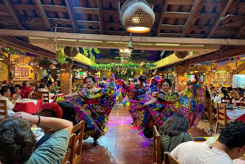 Vibrant carnival parade with colorful floats and performers in crowded indoor venue with decorated ceiling and wooden beams