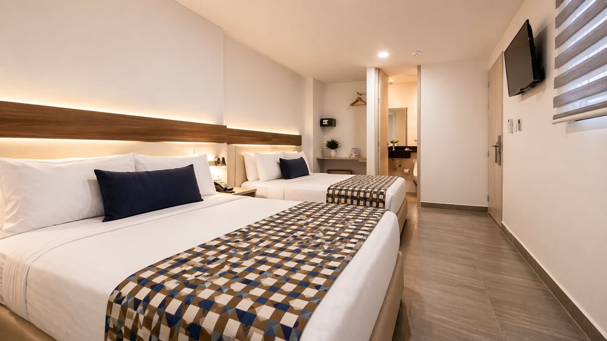Modern hotel room with two queen beds, white bedding, checkered runners, wooden headboard with ambient lighting, and ensuite bathroom