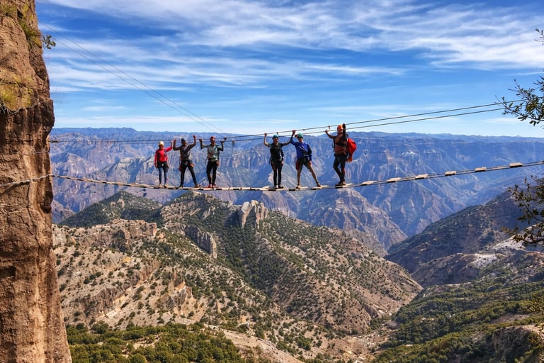 Group of tourists walking on a narrow suspension bridge high above a vast canyon with mountain valley views below