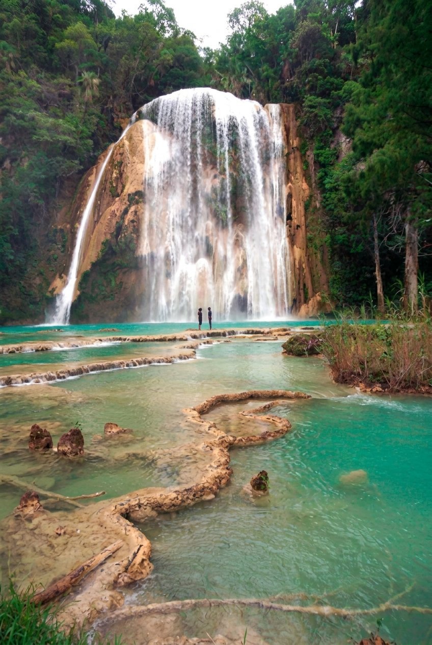 Waterfall cascading into turquoise pool surrounded by lush green forest and limestone cliffs