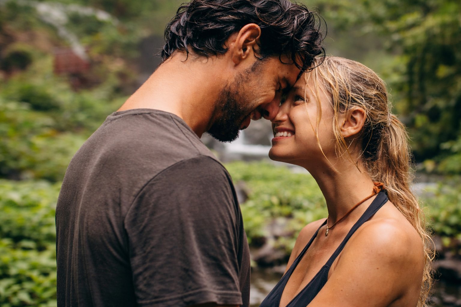 A man and woman smiling face to face outdoors in a lush garden setting, about to kiss