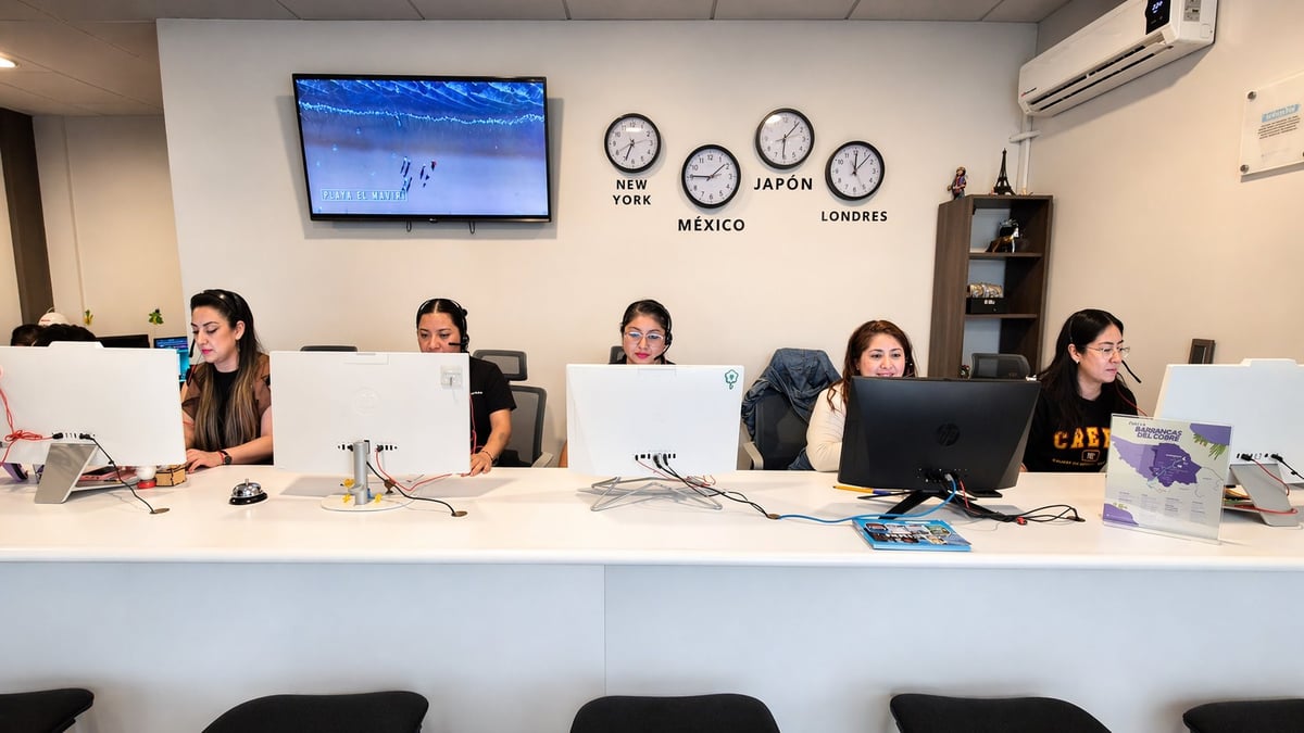 Five women working at reception desk with computers, clocks showing different time zones on wall behind