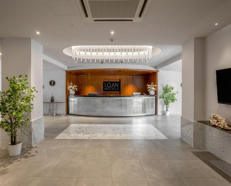 Modern hotel lobby with polished marble floors, wooden reception desk, crystal chandelier, potted plants, and Loan Hotel signage on back wall
