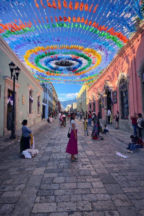 Colorful spiral art installation overhead on a cobblestone street lined with colonial buildings and pedestrians