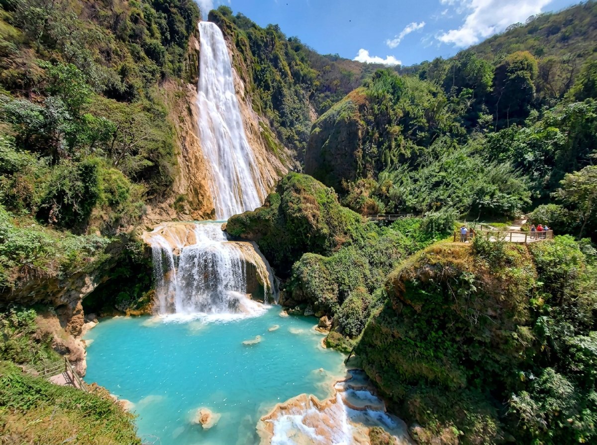 Cascading waterfall flowing into a vibrant turquoise pool surrounded by lush green mountains and vegetation
