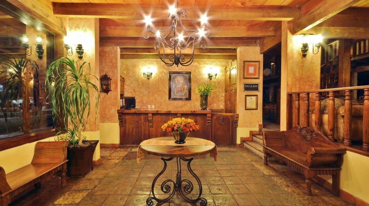 Elegant hotel lobby with warm lighting, wooden beams, ornate chandelier, round table with wrought-iron base, and upholstered seating