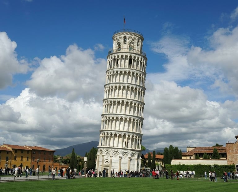 The Leaning Tower of Pisa, a historic stone bell tower with distinctive tilted architecture, surrounded by tourists on green grass under a blue sky with white clouds