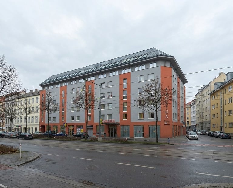 Modern apartment building with orange and gray facade on an urban street corner with surrounding older buildings and overcast sky