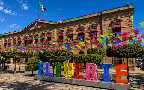 Colorful QUERÉTARO sign in front of historic brick government building with Mexican flag and decorative banners under blue sky