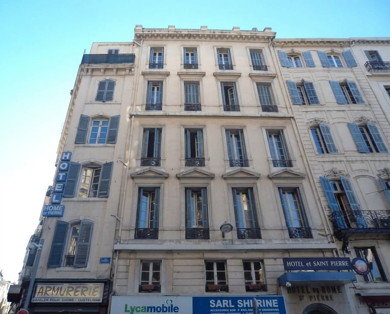 Parisian apartment building facade with cream and blue shuttered windows and ground floor shops against clear blue sky