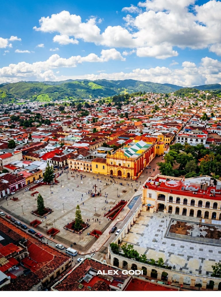 Aerial view of colonial-era town with yellow cathedral, red-tiled buildings, and green mountains under blue sky