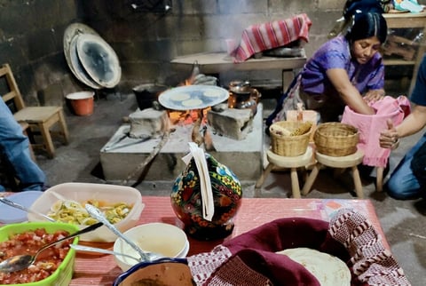 Women preparing and serving traditional Asian food in a rustic kitchen with various dishes and cooking equipment visible