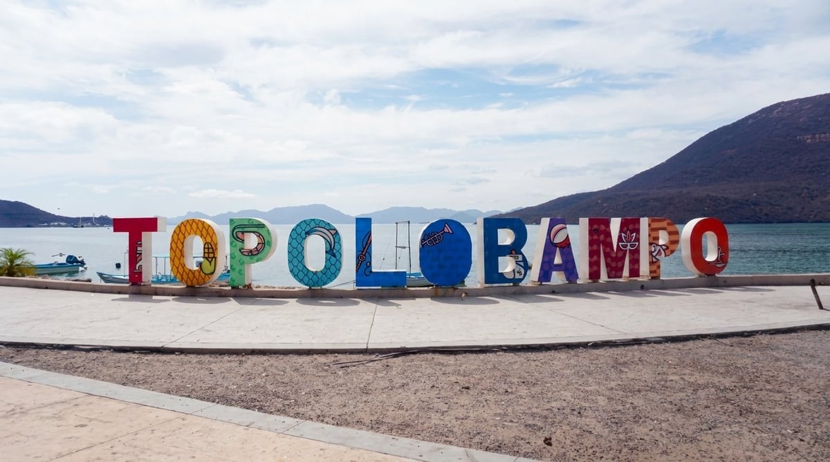 Colorful TOPOLOBAMPO sign on a beach with mountains and water in the background