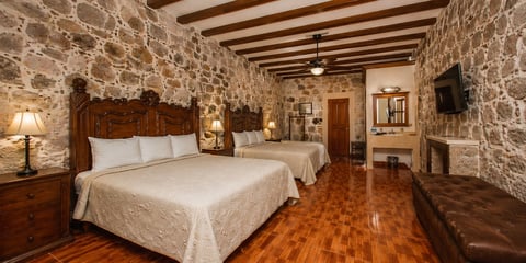 A hotel bedroom with two beds, wooden beams, stone walls, and warm wooden flooring