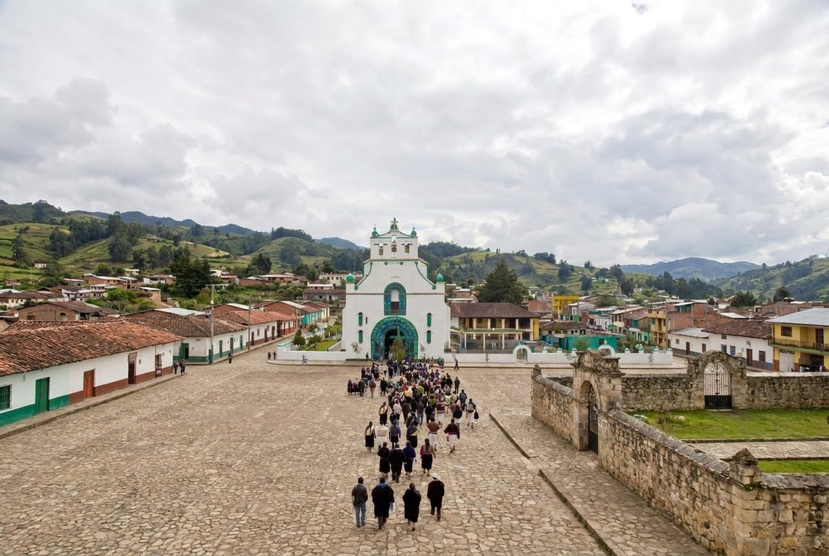 Colonial town square with white church, green dome, stone plaza, tourists, and mountains in background