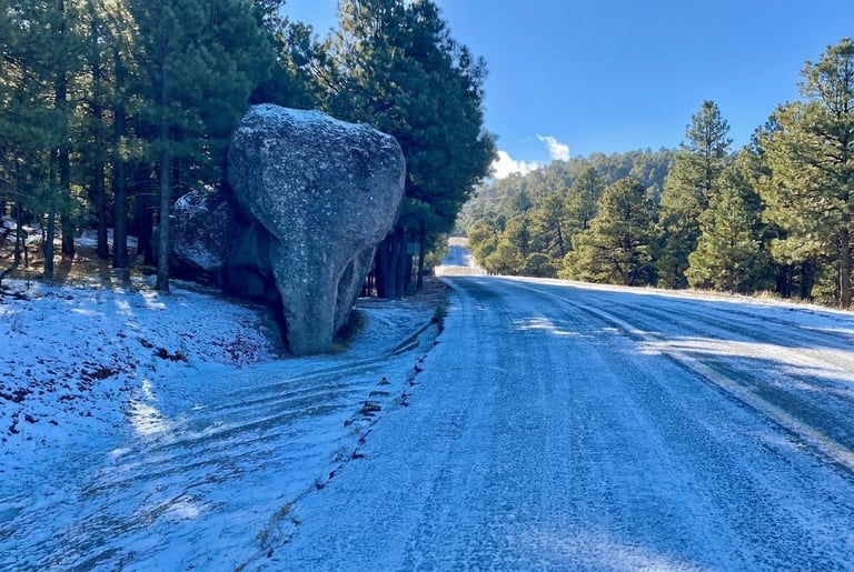 Large balanced boulder on snowy roadside with forest and clear sky in background