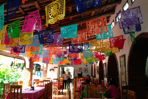 Colorful papel picado decorations hanging from wooden ceiling beams in a rustic Mexican restaurant interior