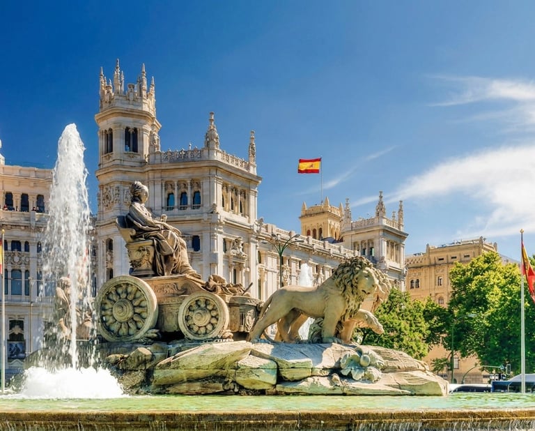 Ornate bronze fountain sculpture with clock wheels in Madrid plaza, featuring historic palace and fountain spray against blue sky