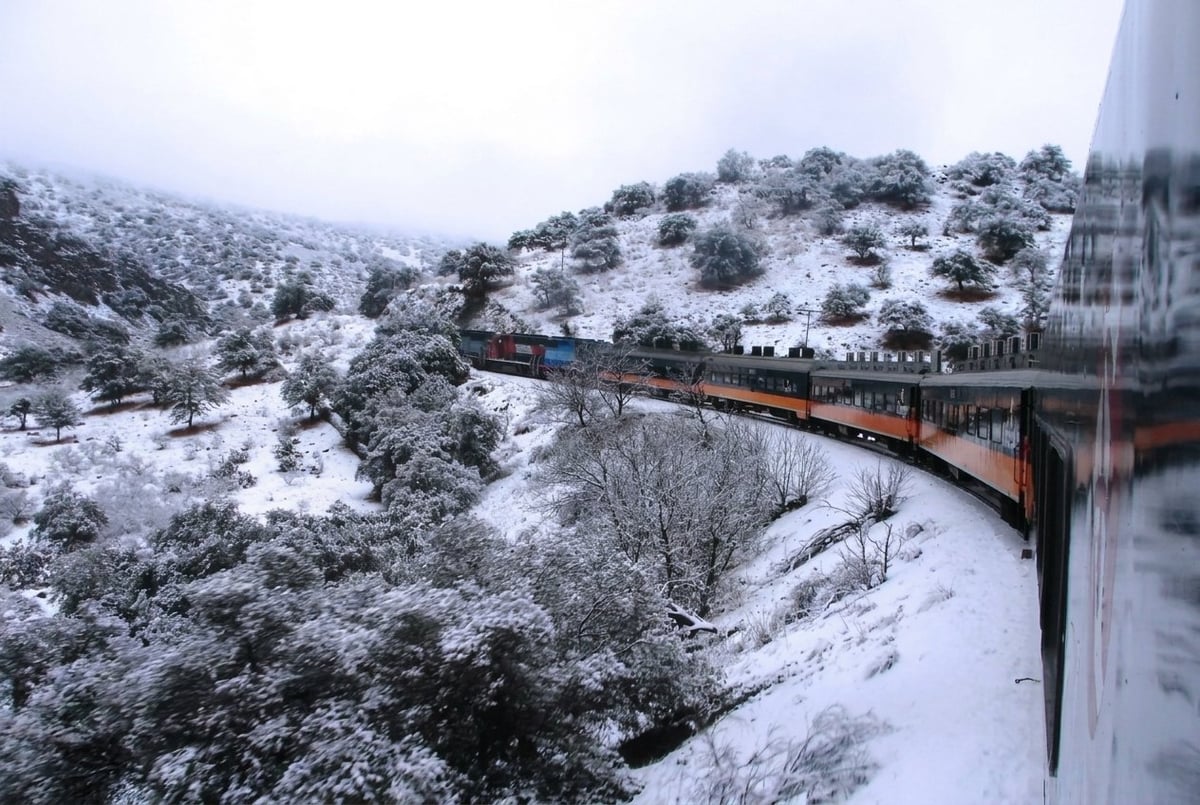 Vintage train traveling on curved tracks through snowy mountainous terrain with snow-covered hills and evergreen trees