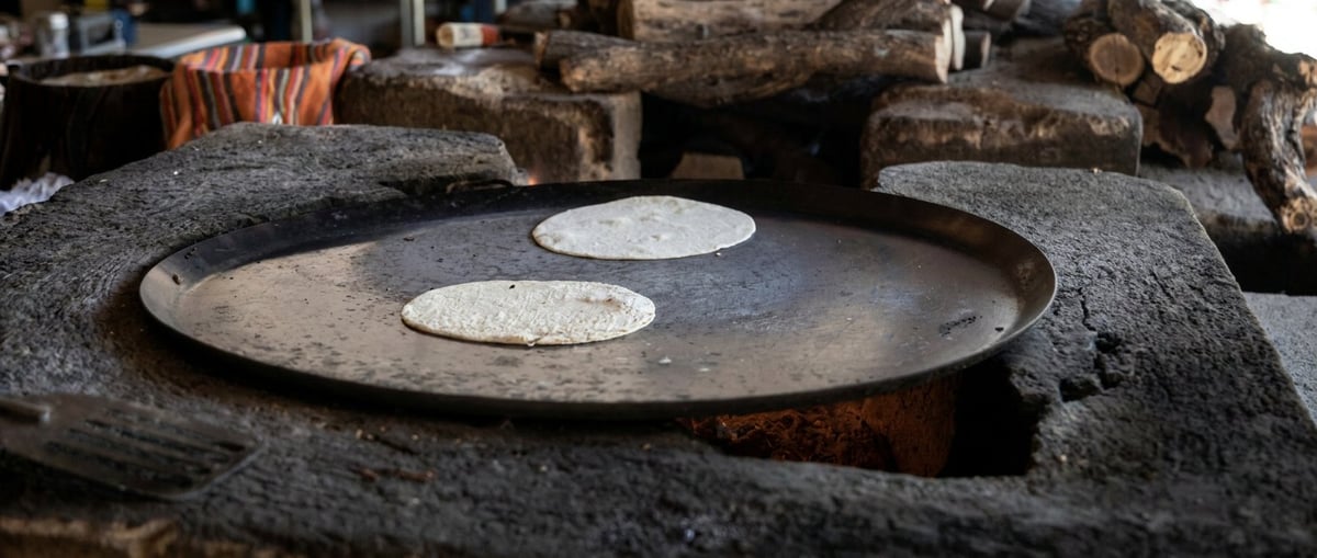 Large circular metal pan with two white circles on a gray stone surface, with logs in the background