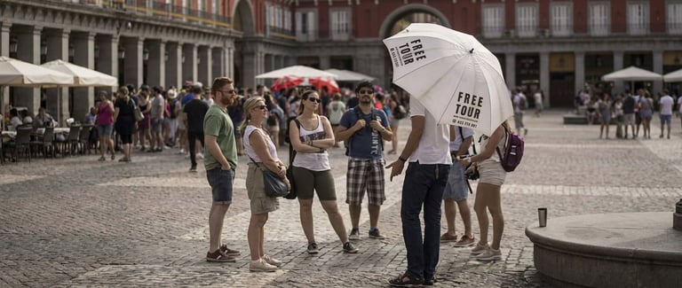 Group of people holding umbrellas in a large European plaza during rainy weather