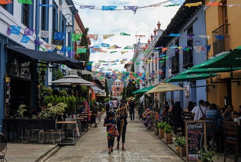 Vibrant colorful street market lined with shops and stalls, colorful flags overhead, people walking through pedestrian alley