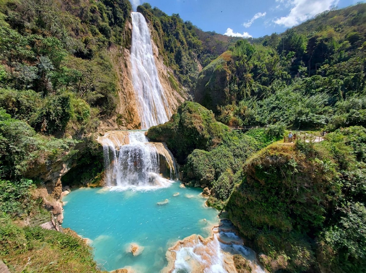 Cascading waterfall flowing into a turquoise pool surrounded by lush green mountains and vegetation