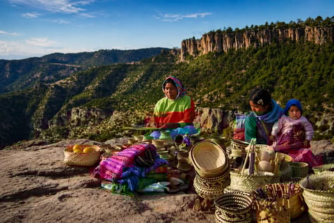 Artisans weaving baskets on a mountain clifftop overlooking a forested valley with dramatic rock formations in the background
