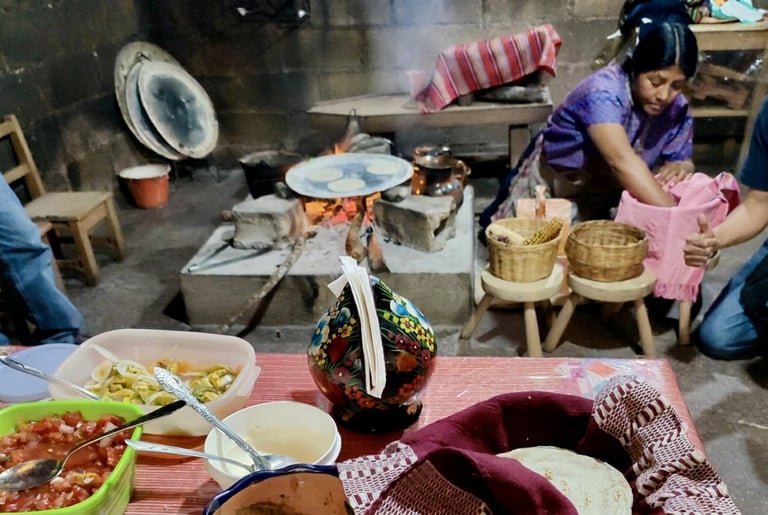 Traditional kitchen scene with woman preparing food, various dishes and bamboo baskets on table, cooking setup in background