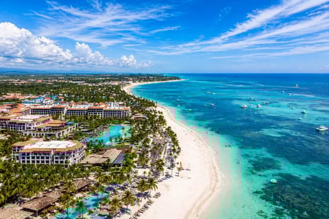 Aerial view of a tropical beach resort with white sand, turquoise ocean, palm trees, and beachfront hotels under blue sky