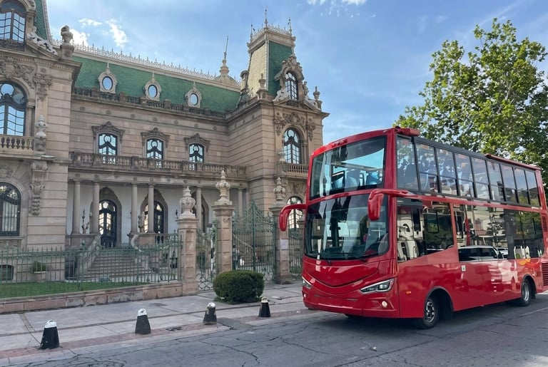 Red double-decker tour bus in front of ornate historic stone building with green roof and turrets