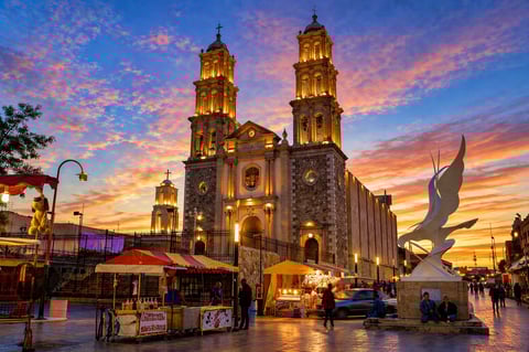 Illuminated cathedral with twin domes at sunset in a plaza