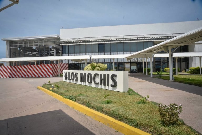 Modern Ojos Mochis building exterior with signage, landscaping, and paved courtyard area under clear sky