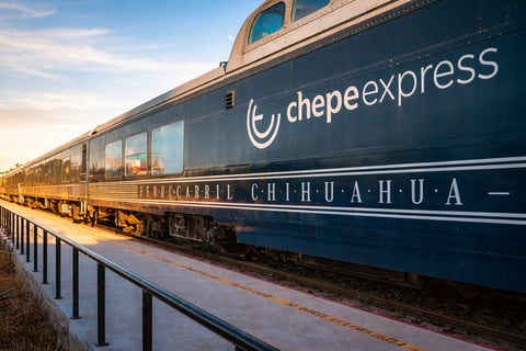 Chepe Express passenger train car displayed at platform with blue and gold livery against sunset sky